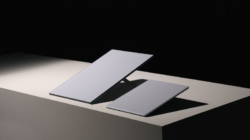 Two slim, light-colored rectangular devices in tilted stands rest on a flat surface against a dark background under a single beam of light.