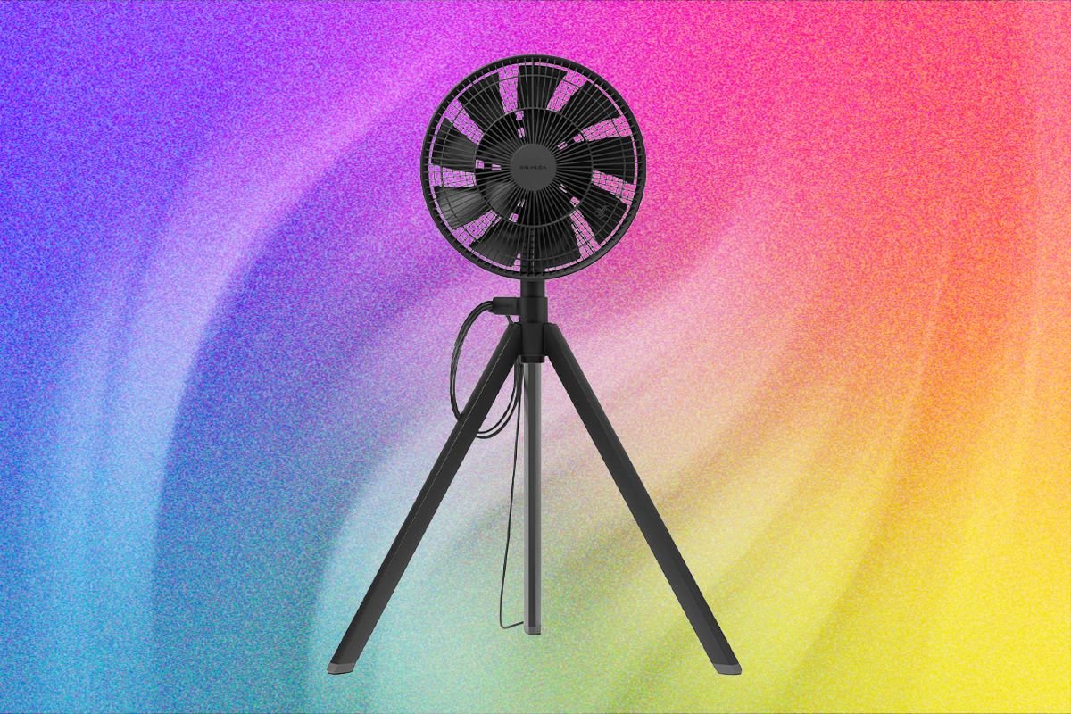 A black circular electric fan mounted on a tripod stand is displayed against a colorful gradient background blending pink, purple, blue, and yellow hues.