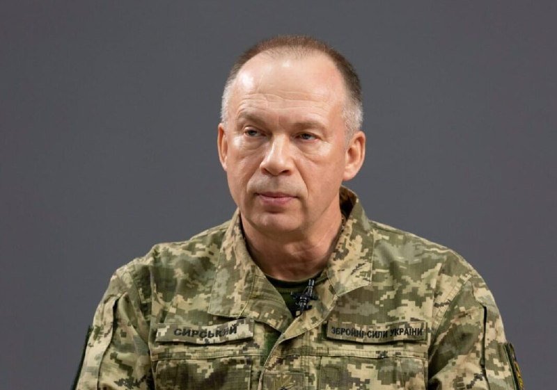 A gray-haired man in a Ukrainian military camouflage uniform with "ЗБРОЙНІ СИЛИ УКРАЇНИ" patches speaks against a plain gray background.