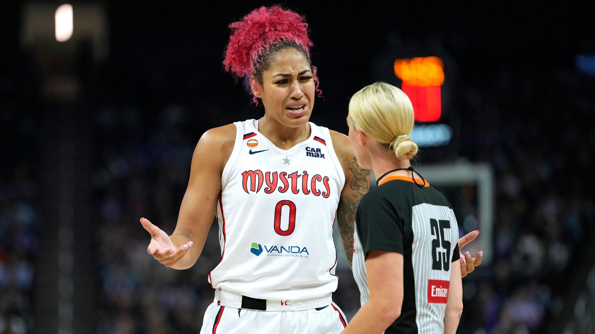 A Washington Mystics basketball player in a white #0 jersey gestures with both hands while speaking to a referee in a black and white striped shirt.