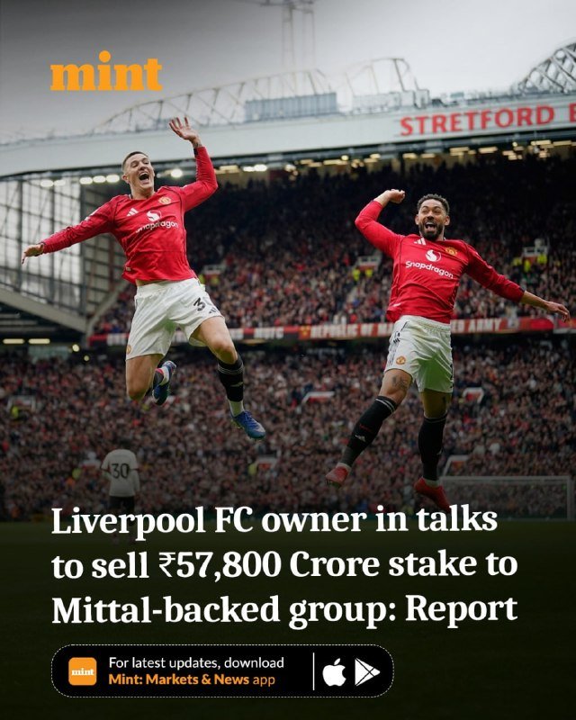 Two soccer players in red jerseys celebrate mid-air in front of a packed stadium crowd at Old Trafford.