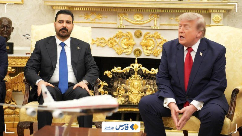 Two men in dark suits sit in ornate gold chairs in an elaborately decorated room, one with a beard and blue tie, the other with blonde hair and a red tie.