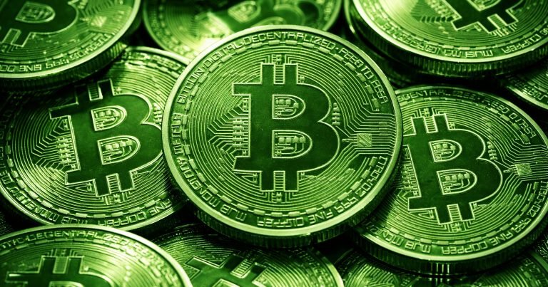 A close-up photograph shows a pile of green-tinted physical Bitcoin tokens with circuit-like designs and inscriptions such as "BITCOIN DIGITAL DECENTRALIZED PEER TO PEER."