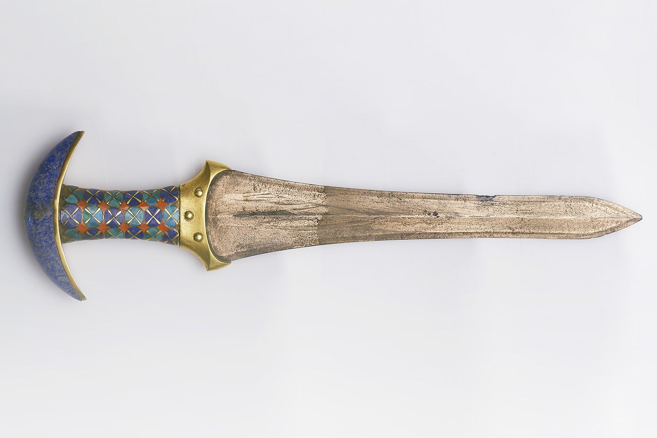 A short sword with a metal blade, brass fittings, and a blue enameled hilt featuring a geometric pattern rests against a white background.