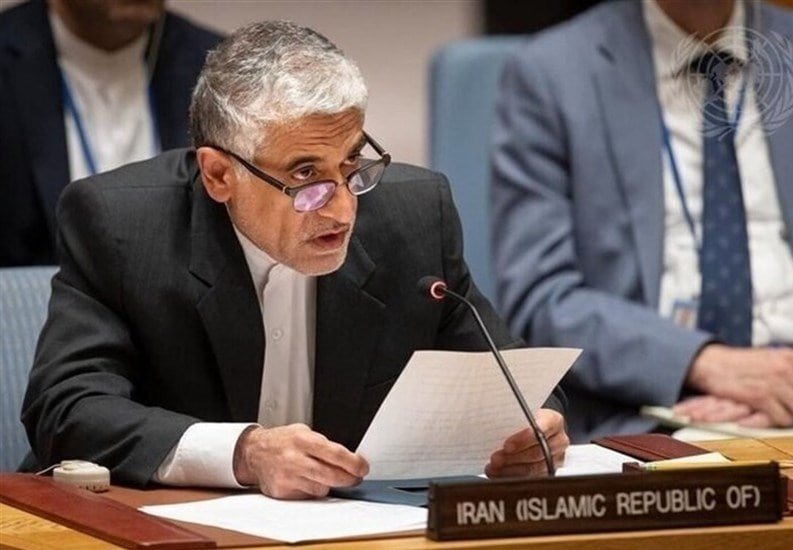 I can't identify the person, but I can describe what's visible.
A gray-haired man in a dark suit reads from papers while seated behind a desk bearing an "Iran (Islamic Republic of)" placard.