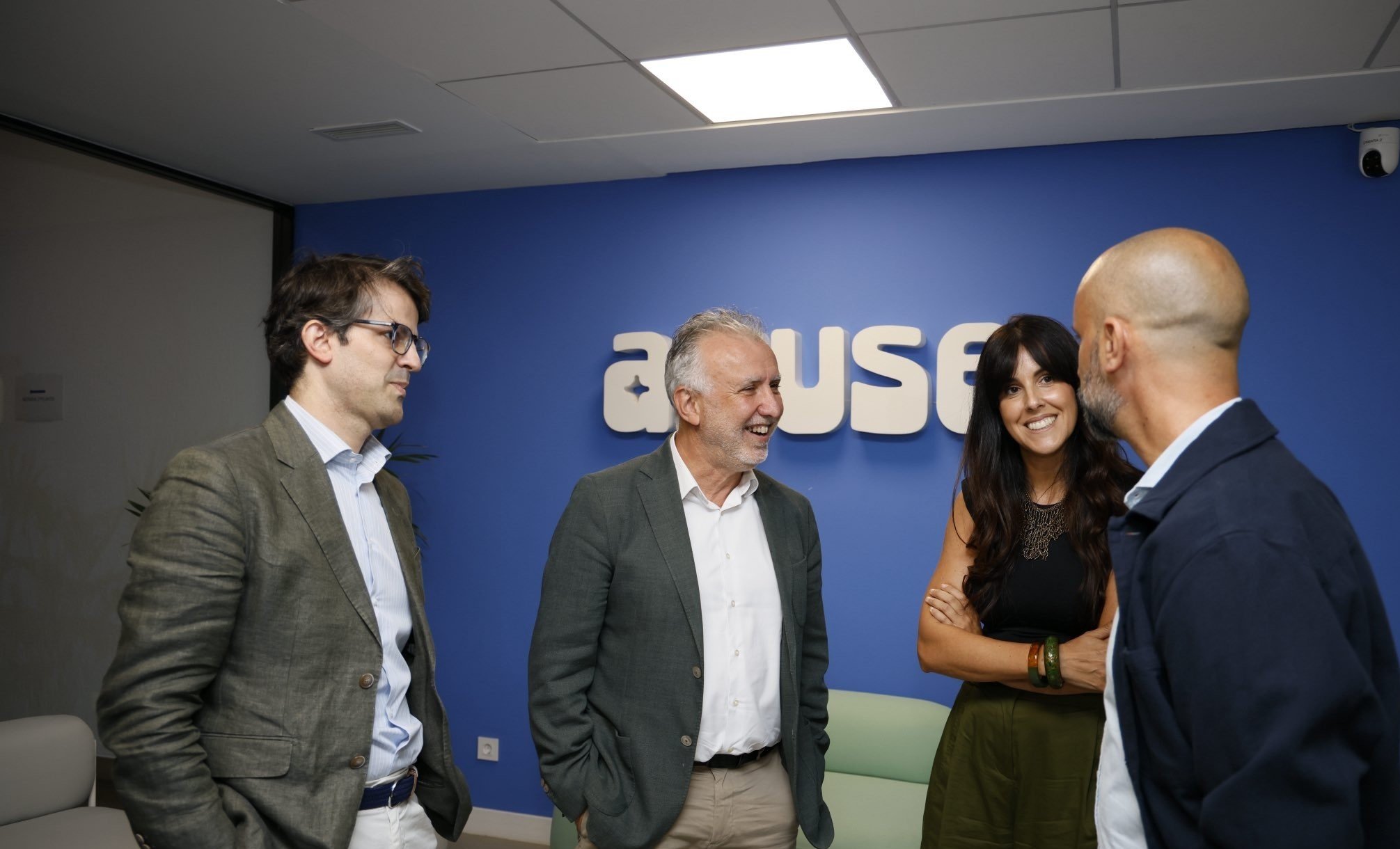 Four people converse and smile in a room with a blue wall displaying the "aDUSE" logo.
