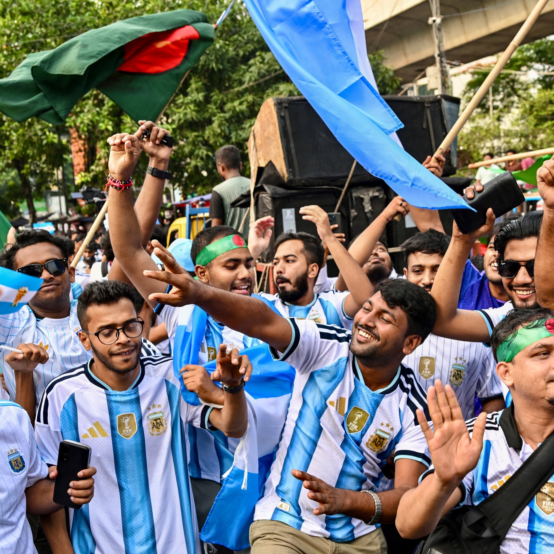 Young men wearing Argentina football jerseys cheer and wave flags in a crowd.