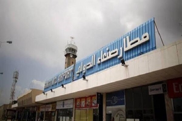 A blue and white "Sana'a International Airport" sign in English and Arabic tops a terminal building, with a control tower rising behind it under an overcast sky.