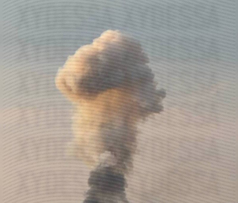 A photo shows an explosion with a mushroom-shaped smoke plume rising into a pale sky, viewed through a screen.