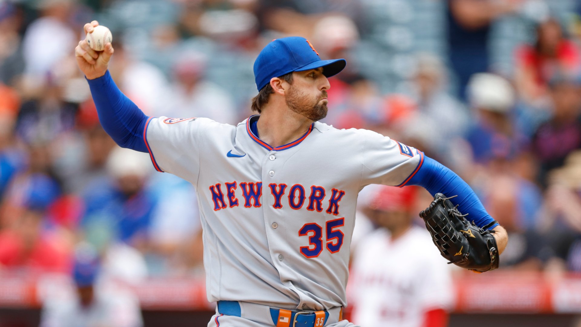 A baseball player wearing a New York jersey with the number 35 throws a pitch during a game, with spectators visible in the blurred background.