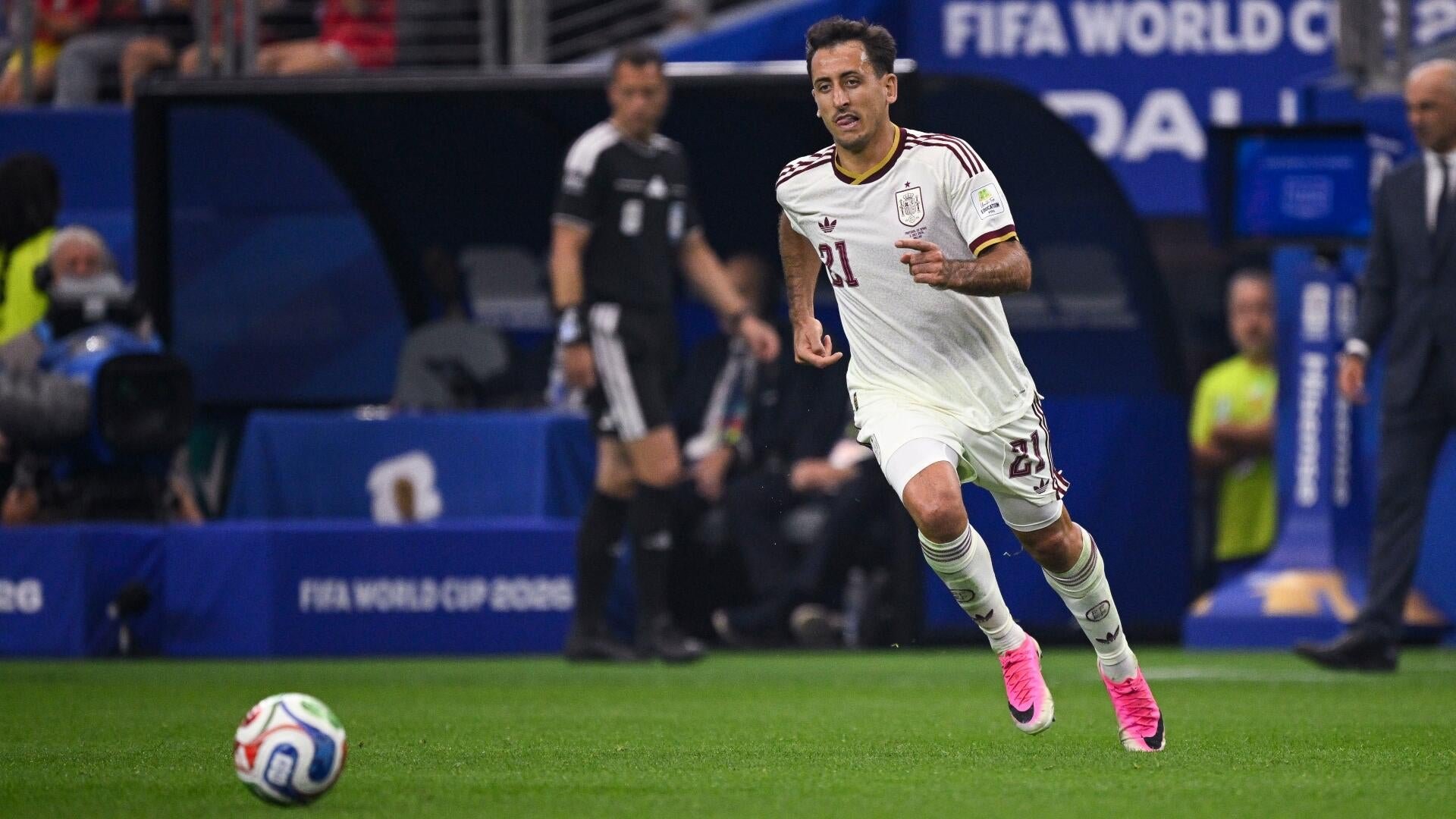 A soccer player in a white jersey with the number 21 runs toward a ball on a green field during a FIFA World Cup match.