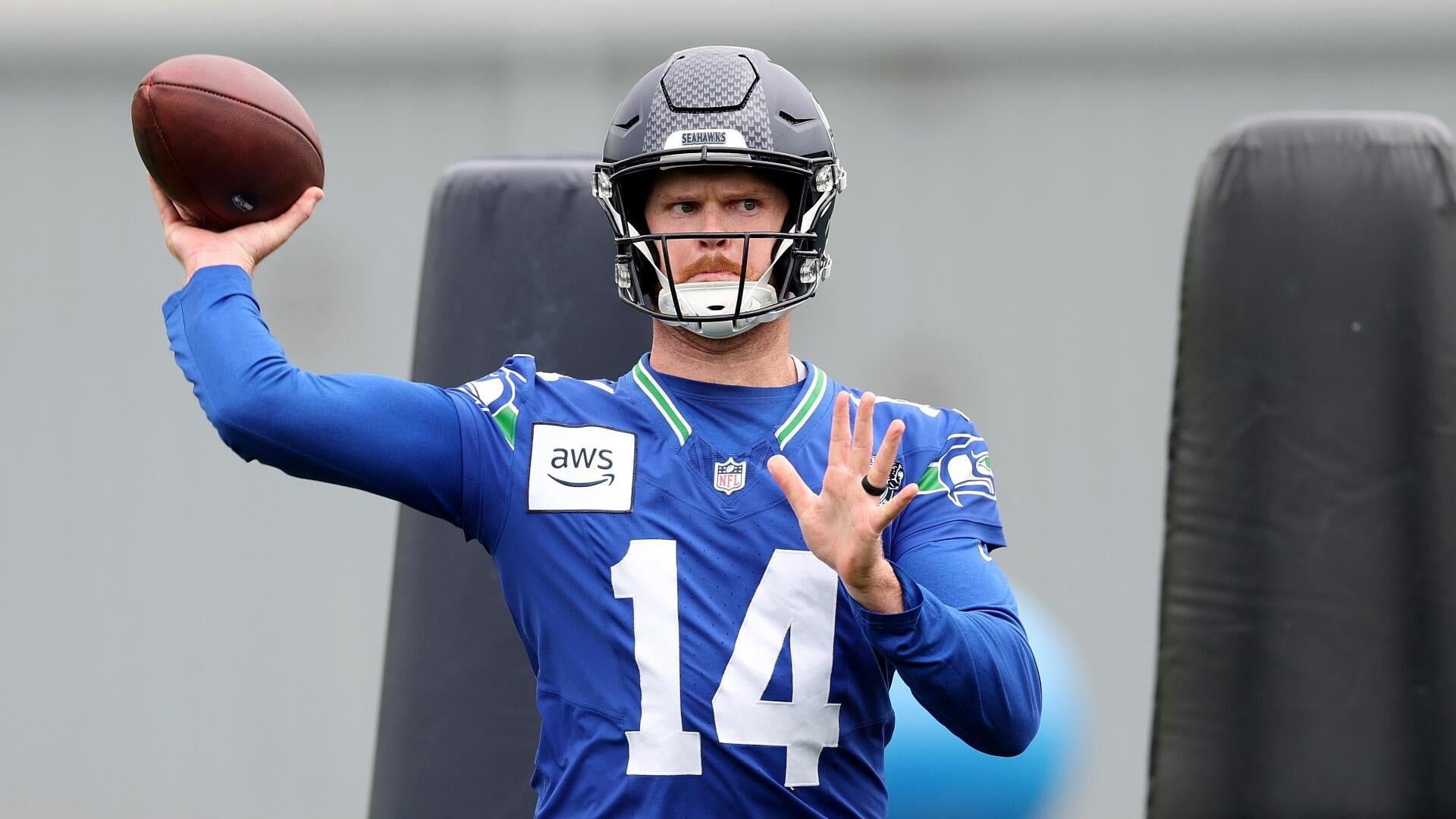 A football player wearing a blue Seattle Seahawks jersey with the number 14 and a helmet prepares to throw a football during practice.