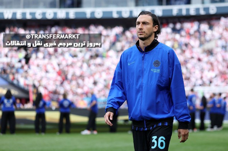 A bearded man in a blue Inter Milan tracksuit stands on a football pitch, with other players in similar attire visible behind him and a crowded stadium in the background.