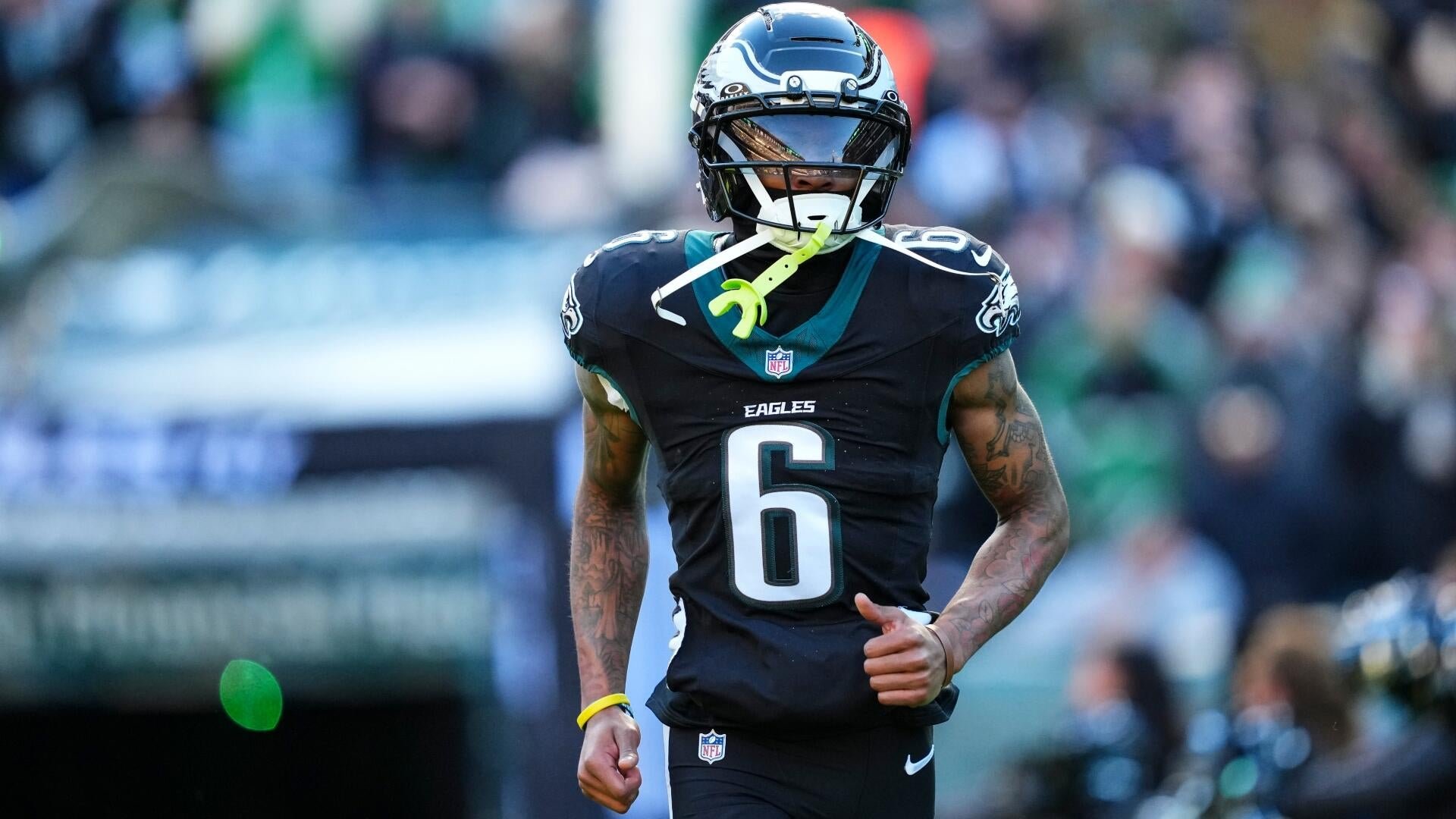 An Eagles player wearing number 6 walks off the field in a black jersey and helmet, holding a mouthguard, with blurred fans visible in the stands behind him.