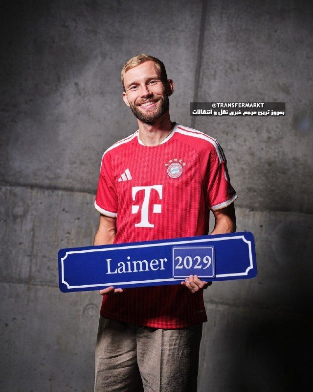 A smiling man in a red FC Bayern Munich jersey holds a blue sign reading "Laimer 2029," with "@TRANSFERMARKT" and Arabic text visible above.