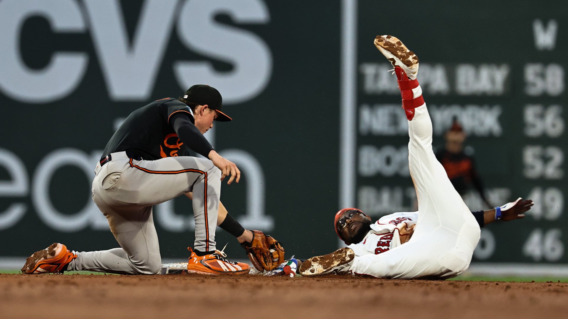 A baseball player in a white uniform slides into a base feet-first while a fielder in a black and gray uniform kneels with his glove ready to tag him.