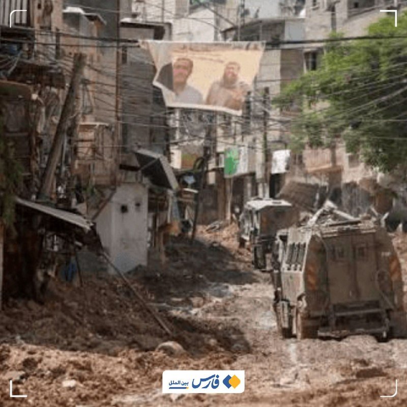 A muddy street is filled with debris and sludge, with an armored vehicle parked on the right and a banner bearing two portraits hanging between damaged buildings.