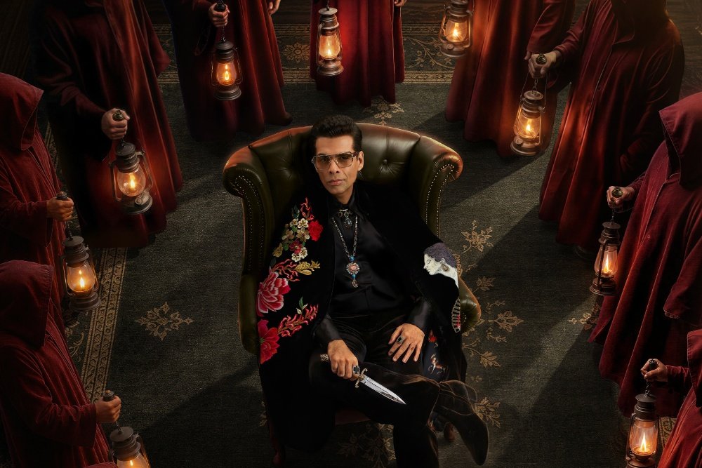 A man in sunglasses and an embroidered black coat sits in a green leather armchair, holding a dagger, surrounded by hooded figures in red robes holding lit lanterns.