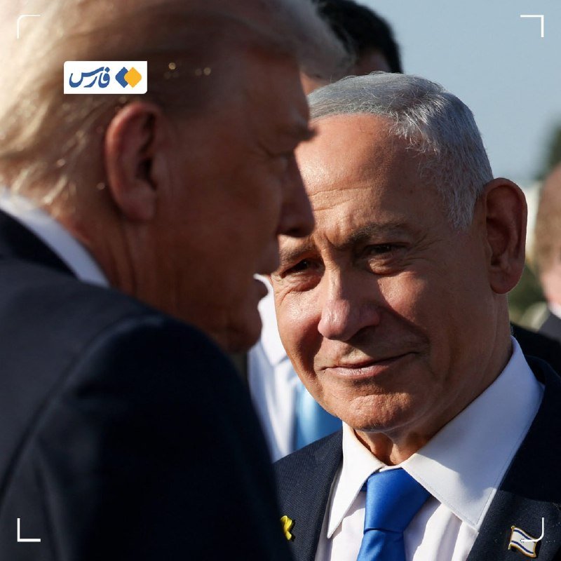 A gray-haired man in a dark suit, white shirt, and blue tie with a yellow ribbon pin stands facing another man in a dark suit, with additional people visible in the background.