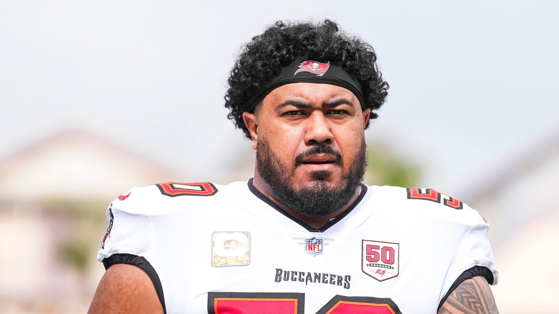 A bearded football player wearing a white Tampa Bay Buccaneers jersey with a "50 Seasons" patch and a black team headband looks off-camera.